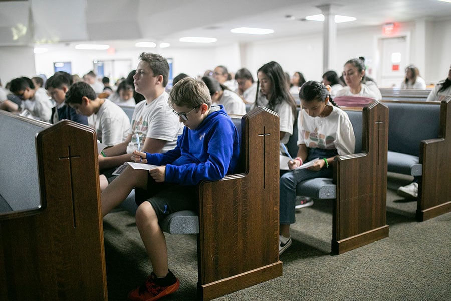 kids write in jounals on pews in Church